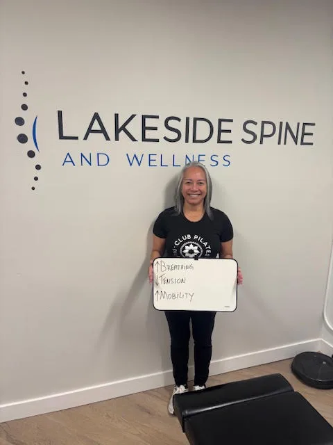 Lakeside Spine and Wellness patient holding a sign: breathing up, tension down, mobility up